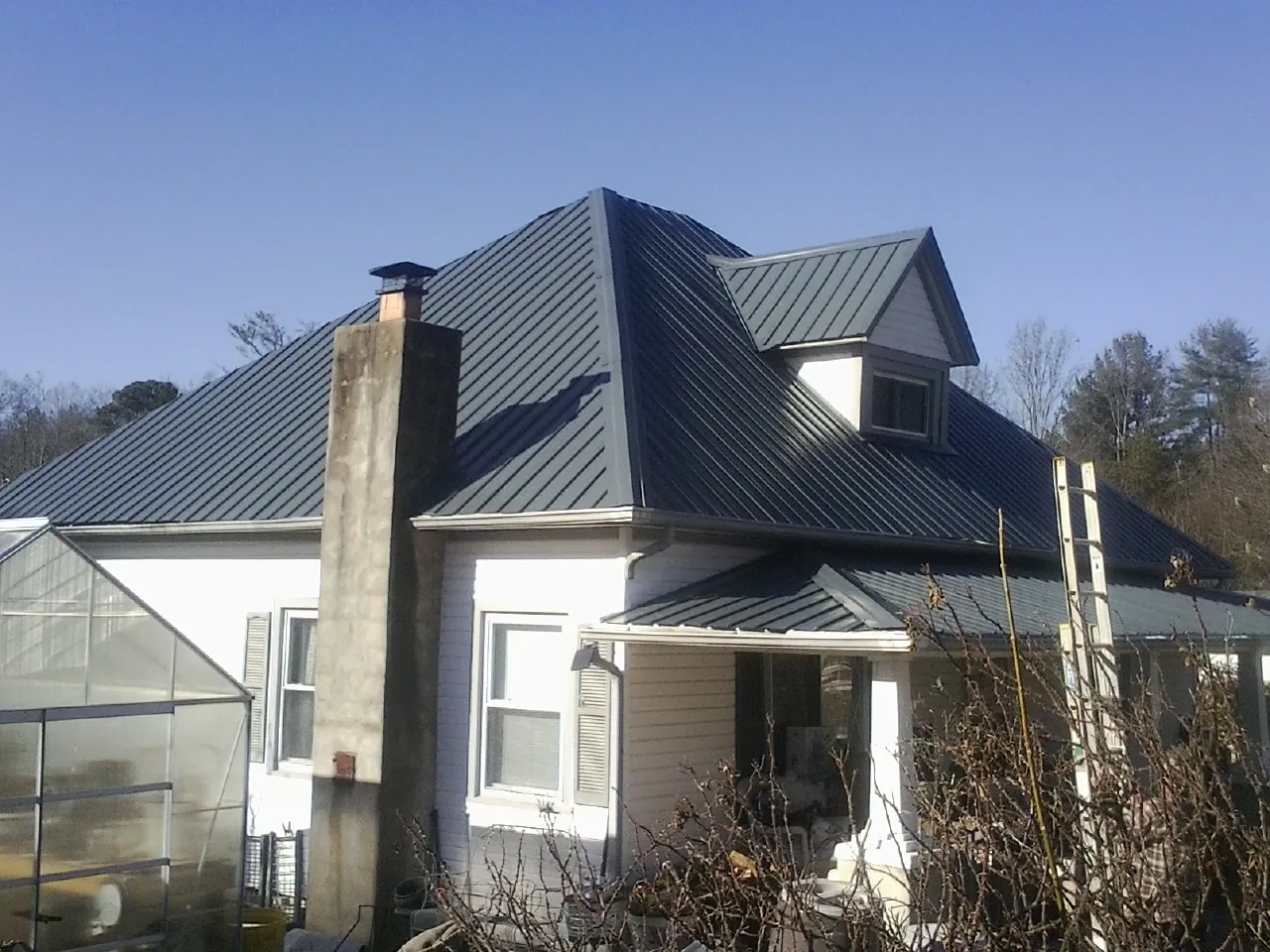 Dark blue standing seam metal roof on a white farmhouse with dormer — Slate & Tile Roof Repair by Roofing Brothers in Hendersonville