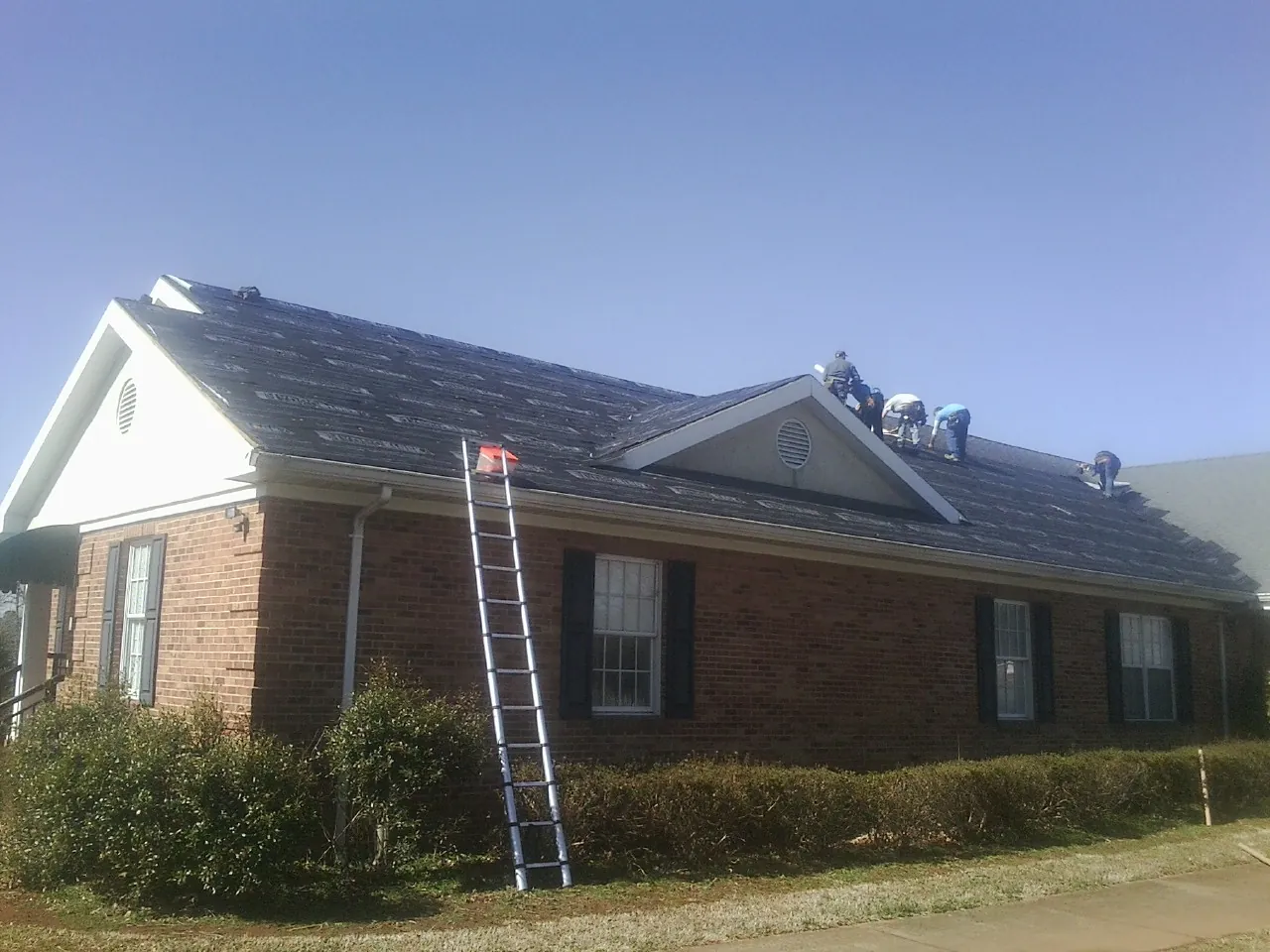 Crew tearing shingles off a brick ranch roof with a ladder set — Metal Roof Repair work by our crew in Hendersonville