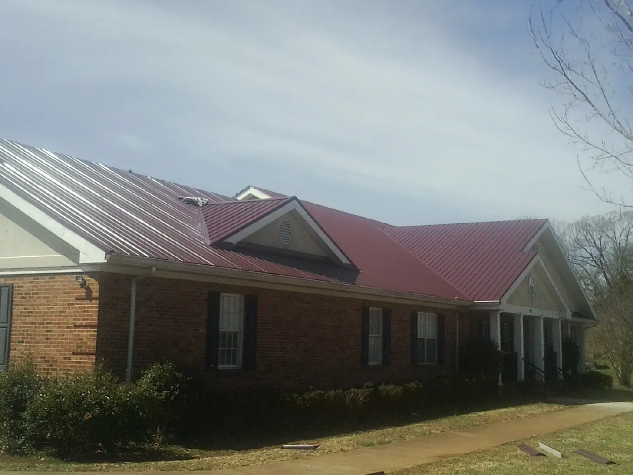 Red metal roof with gabled entries on a long brick building, from a Hail Damage Roof Repair job in Hendersonville