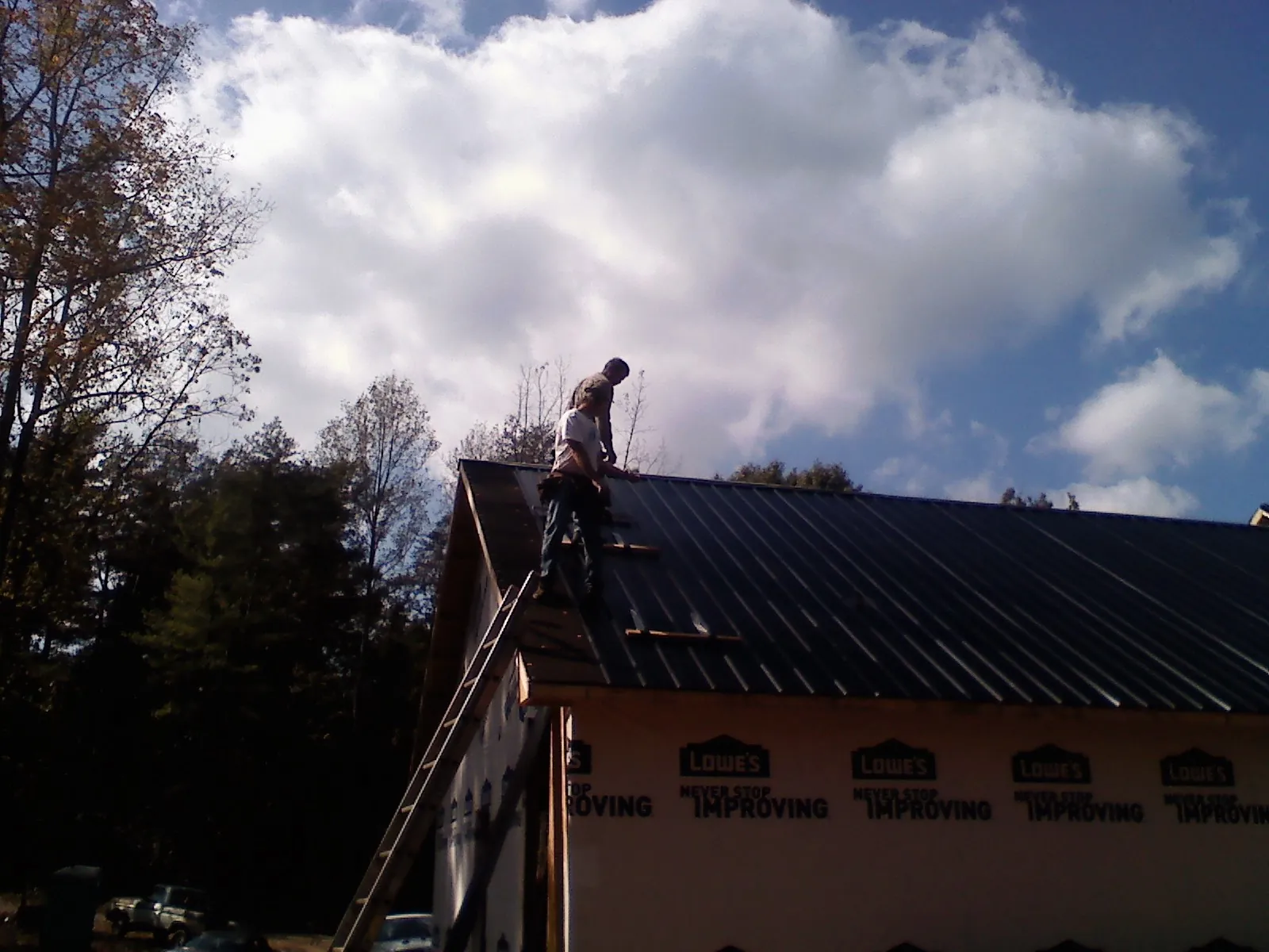 Roofer fastening dark metal panels high against a cloudy sky, from a Roof Inspection job in Hendersonville