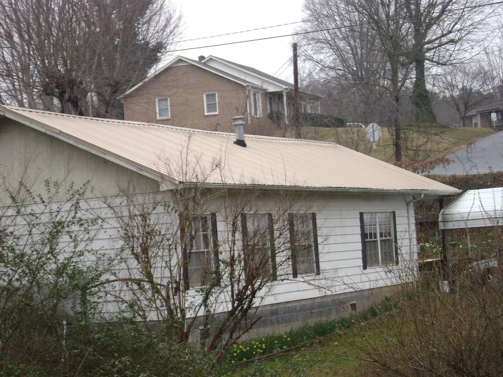 Tan metal roof on a white sided house set into a hillside — Commercial Roofing by Roofing Brothers in Hendersonville